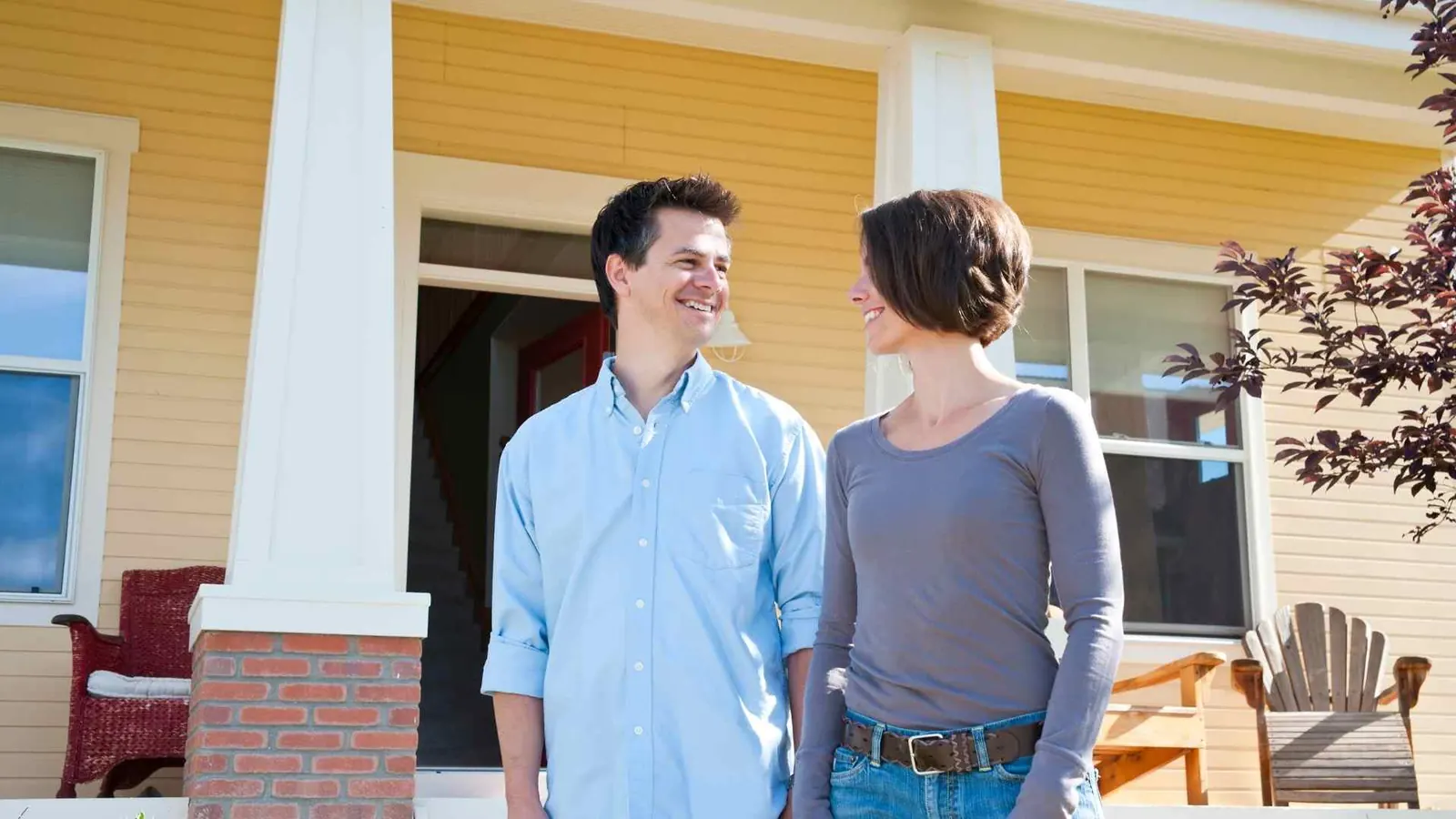 A couple holding hands and smiling in front of their yellow painted home